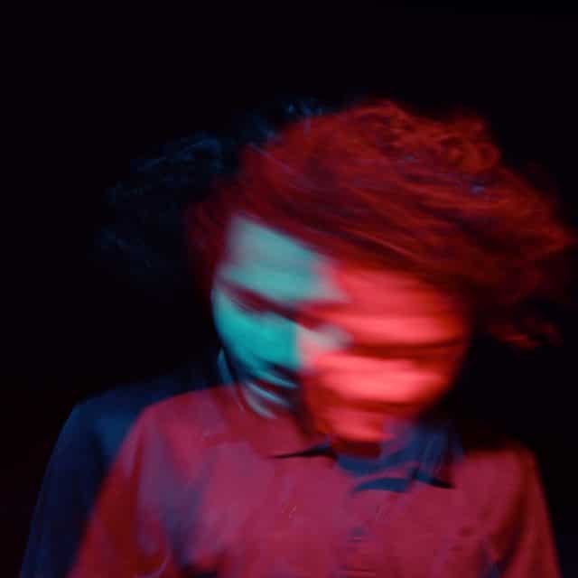 A hazy, psychedelic image of a man in a shirt, moving his head from side to side, taken with slow shutter speed evoking a sense of confusion
