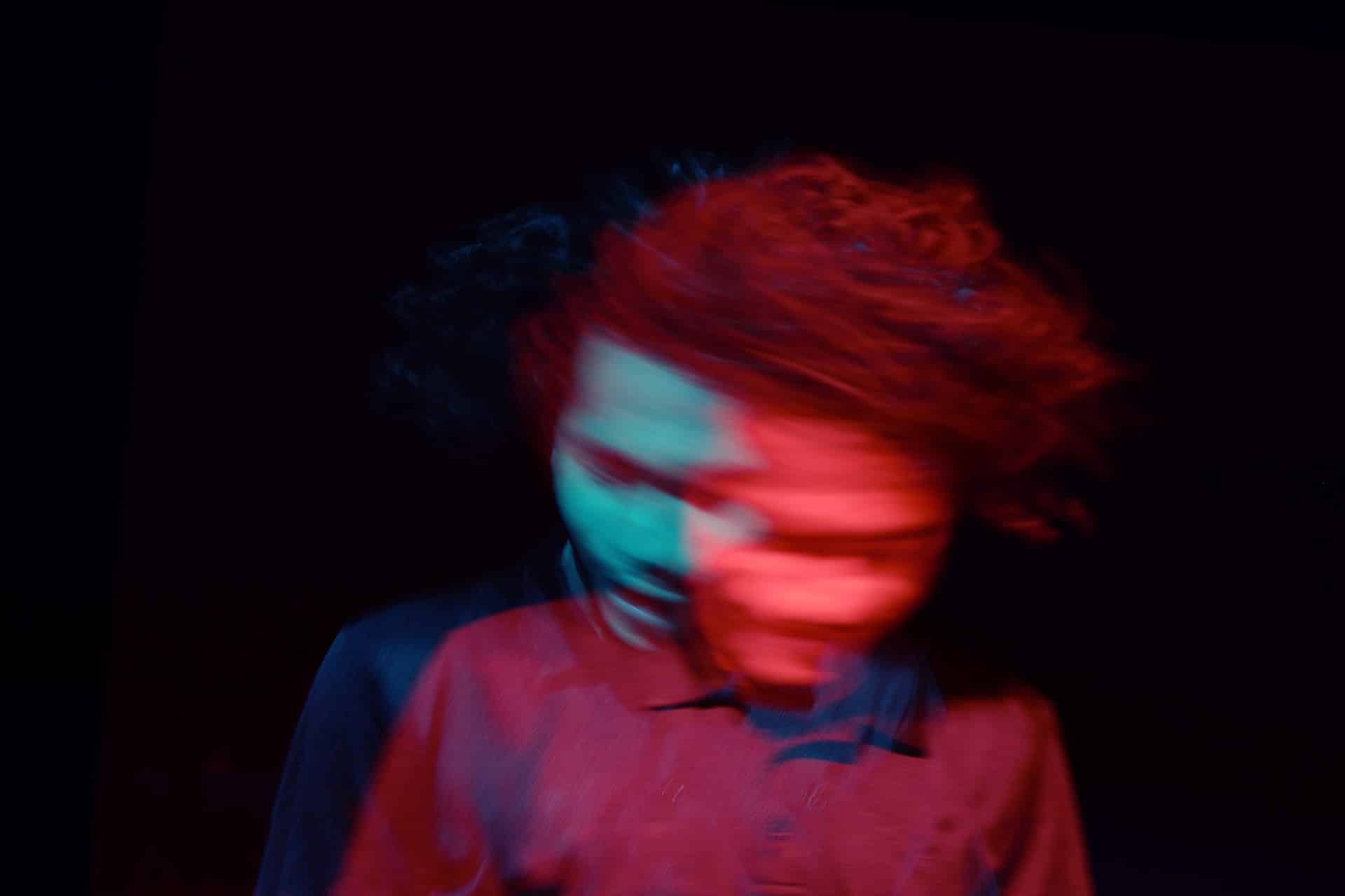 A hazy, psychedelic image of a man in a shirt, moving his head from side to side, taken with slow shutter speed evoking a sense of confusion