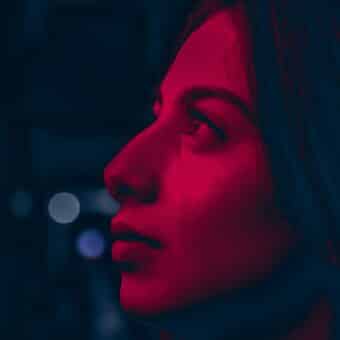 A girl stares into the distance, doused in red light