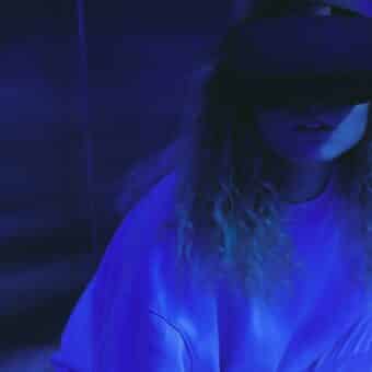A girl in a moody dark room with a virtual reality headset on, looking unsure