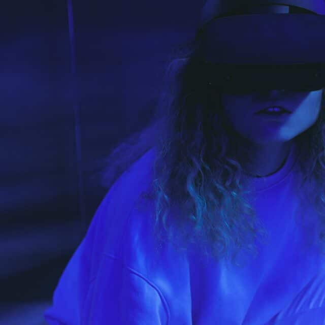 A girl in a moody dark room with a virtual reality headset on, looking unsure