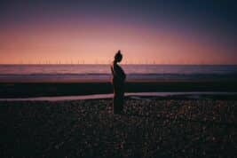 Postnatal Depression Psychologist: A long shot of a pregnant woman in a red dress holding her stomach against a purple and orange sunset