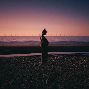 Postnatal Depression Psychologist: A long shot of a pregnant woman in a red dress holding her stomach against a purple and orange sunset