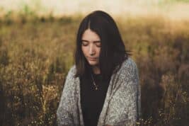 A brown haired girl in a field with a grey cardigan and golden light