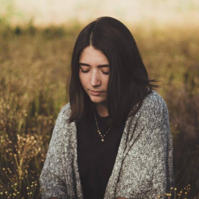 A brown haired girl in a field with a grey cardigan and golden light