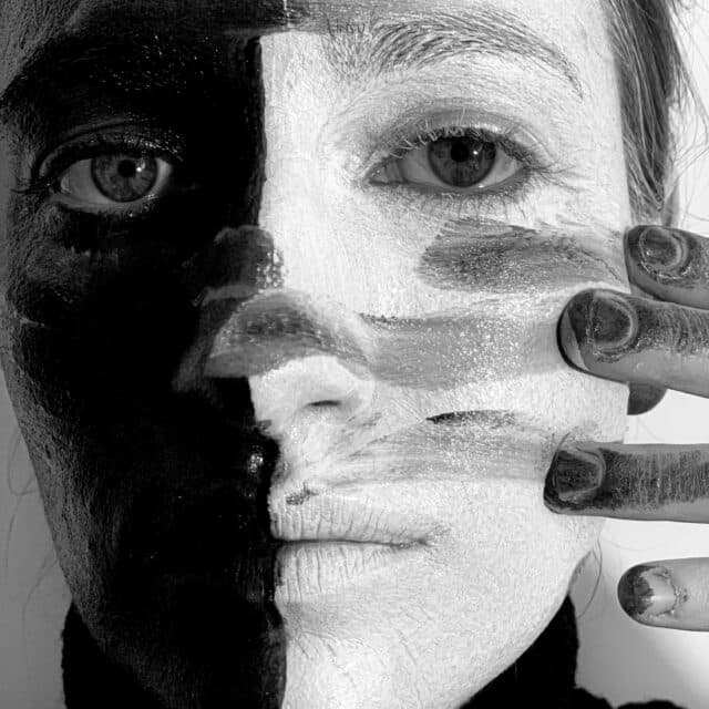 A lady with half her pace fainted white and half painted black, wiping her fingers through the paint