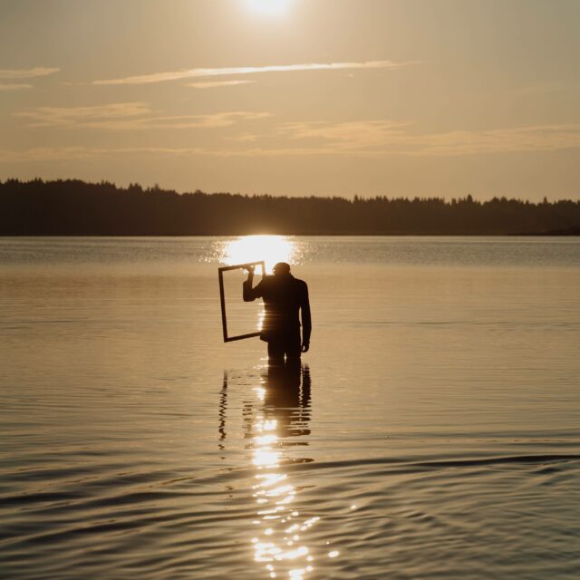A figure walks into the sunset holding a frame