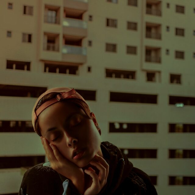 A figure holds their hand against a backdrop of highrise