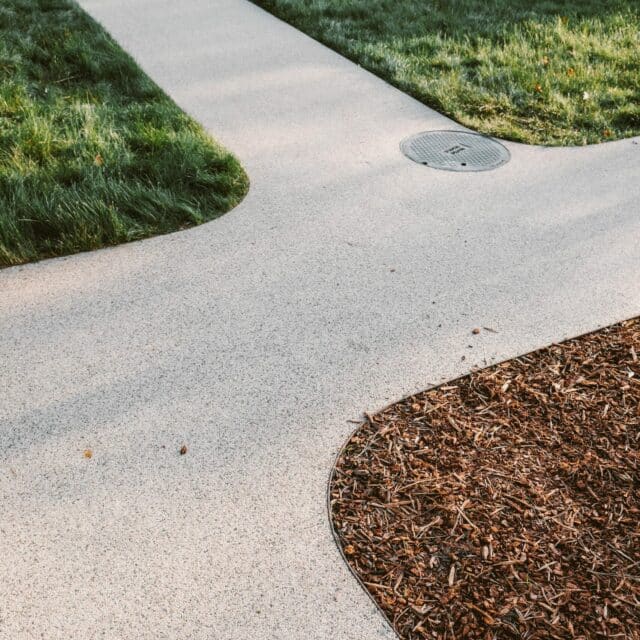 A close up shot of a forked pathway that splits into three different directions. Grass is seen on the upper side of the path while mulch is on the lower right side of the path.
