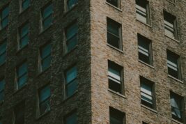 Dialectical Behaviour Therapy: A medium shot of the corner of a building where the sun is shining on one side and the other side is shadowed. The brick building is lined with windows.
