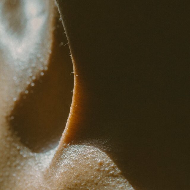 A closeup shot of a strained neck where the neck cartilage creates a strong line against the skin. The sun lights from behind casting shadows.