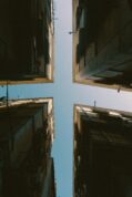 A worms eye view of 4 buildings as their corners intersect against a blue sky to create a cross shape.