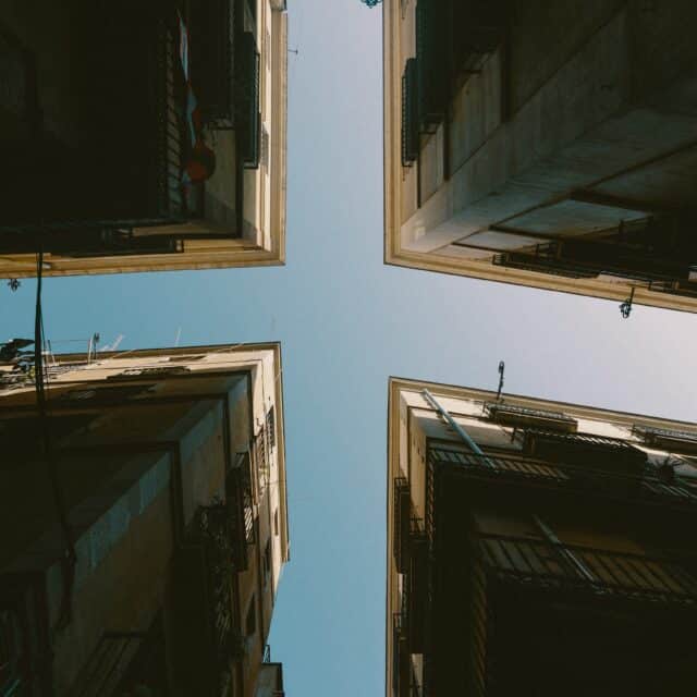 A worms eye view of 4 buildings as their corners intersect against a blue sky to create a cross shape.