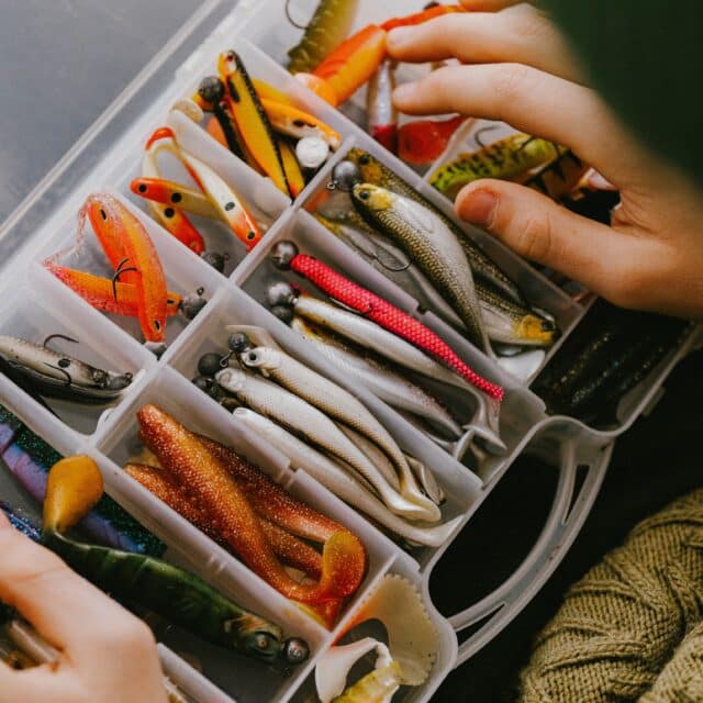 An over the shoulder shot of a fishing bait box in someone's lap with an organised set of fake fish bait.