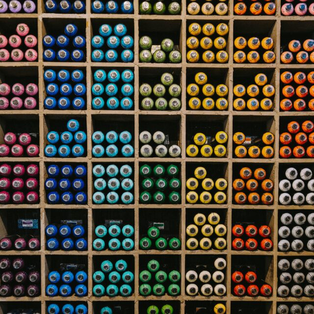 A large wall of square shelves with organised spray cans that are sorted by colour.