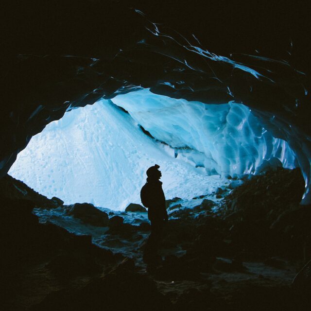 A silhouette of a person at the entrance of an ice cavern looking upwards
