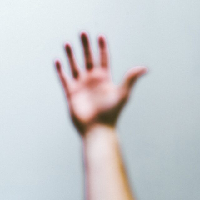 An image of a blurred hand outstretched in front of the camera against a white background.