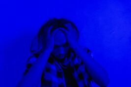 A figure holds their head in blue light